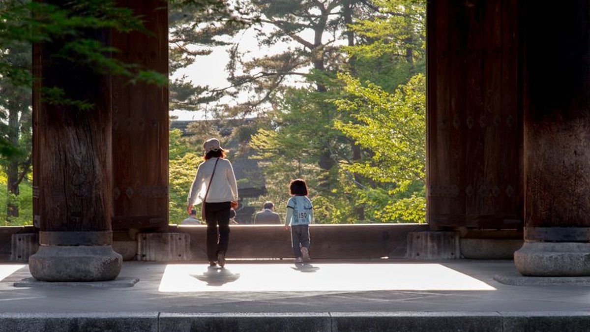 A family strolls through a temple gate surrounded by lush greenery in Kyoto, Japan.