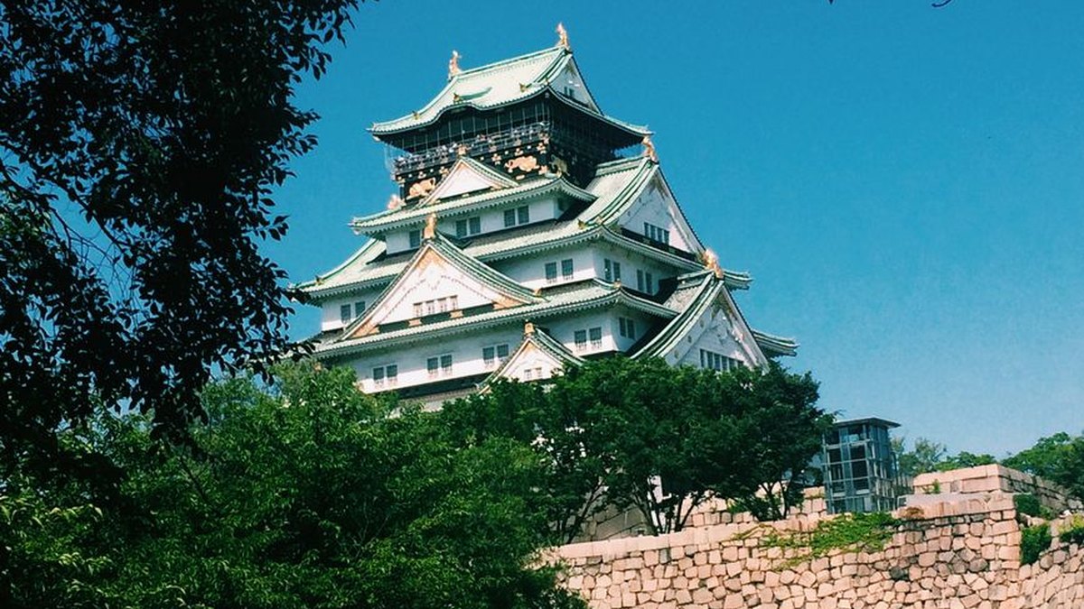 Osaka Castle surrounded by lush greenery under a clear blue sky, captured on a sunny day.