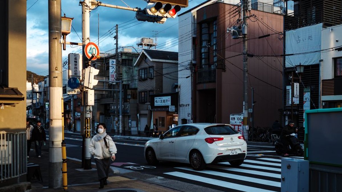 Evening street view in Kyoto, Japan with pedestrians and vehicles at a crosswalk.