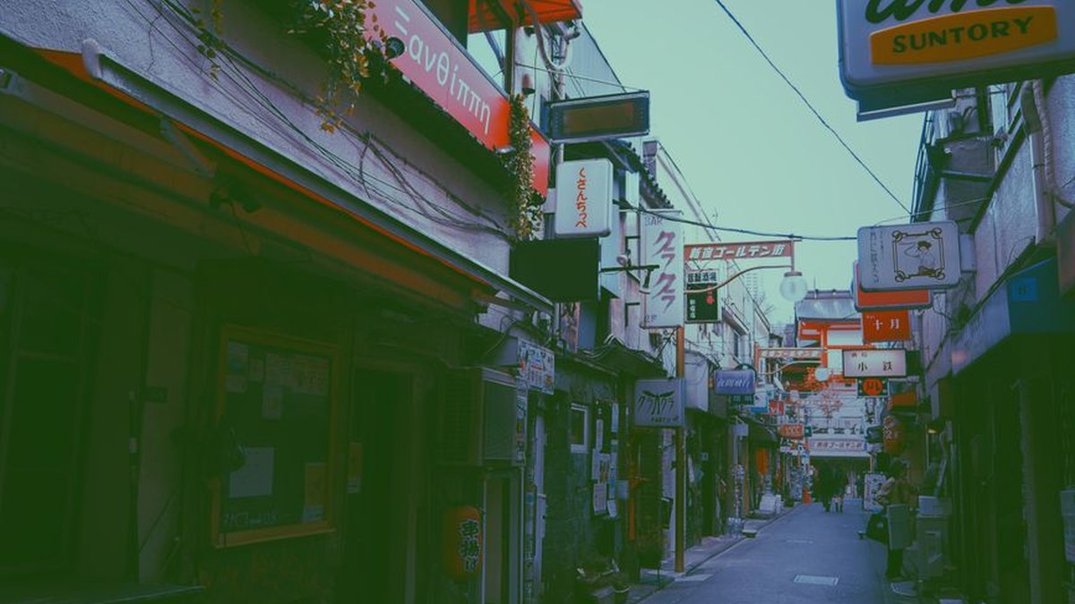 Explore a vibrant, narrow street lined with signs and traditional architecture under clear skies in Japan.