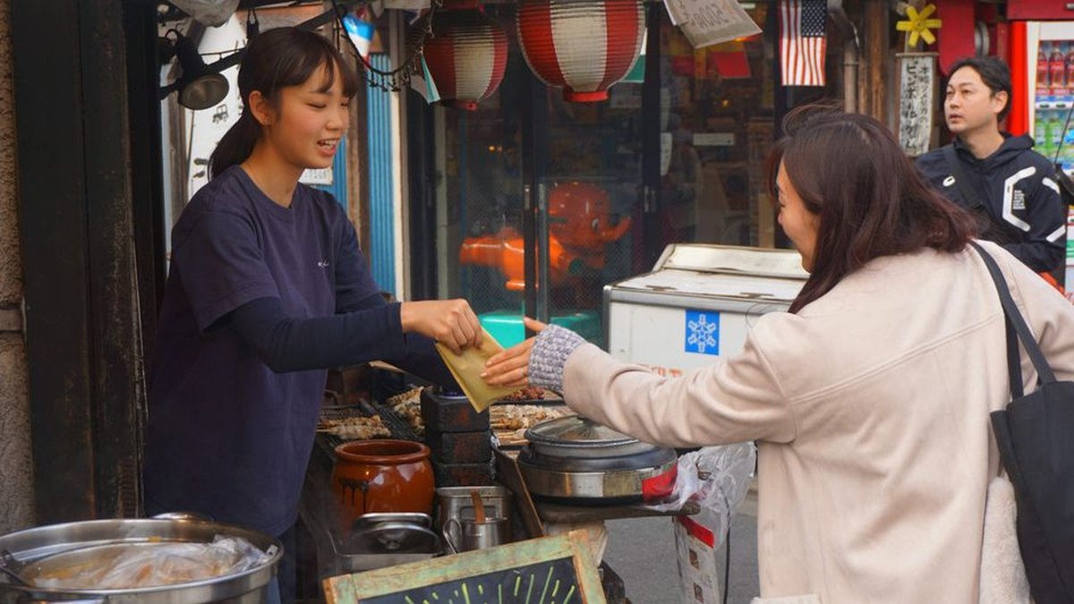 Busy street vendor serving a customer at a lively market stall in Tokyo.