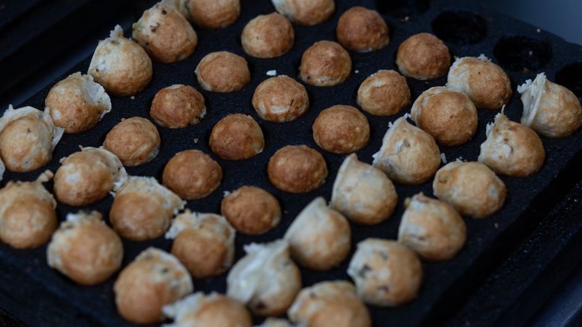 Close-up of Japanese takoyaki balls cooking on a grill, crispy and golden.
